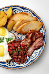 Delicious breakfast plate featuring eggs, beans, bacon, and potato wedges served on a decorative dish