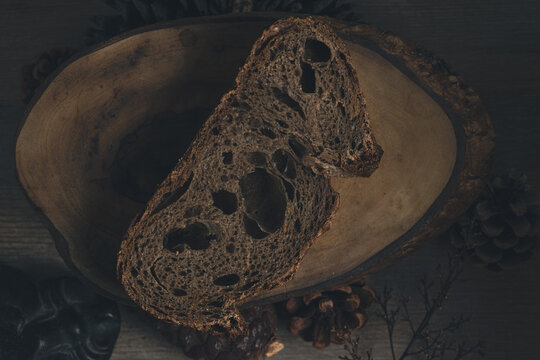 Dark and moody capture of a slice of buckwheat bread on wooden table with cones and dry tree branches emphasizing autumn season