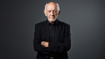 An elderly gentleman in a sharp black suit stands confidently against a neutral backdrop, exuding wisdom and timeless sophistication.