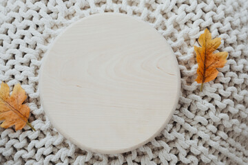 Natural wooden round board on a knitted background with autumn leaves placed around it