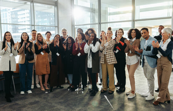 Diverse group of professionals applauding at a conference during corporate training session in a modern office setting
