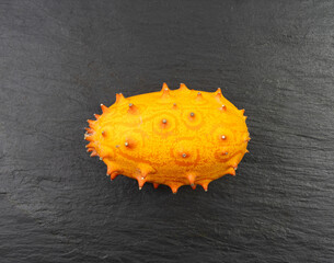 Kiwano on black plate, jelly melon, cucumis metuliferus ripe fruit, orange spiked horned melon