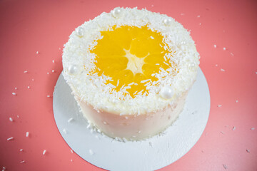 Delicious white chocolate cake decorated with orange and coconut flakes on pink background