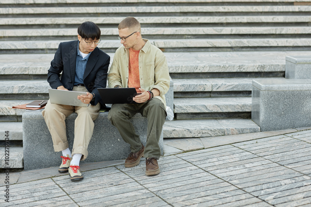 Poster full shot of asian male it developer using laptop collaborating with colleague on work while writing