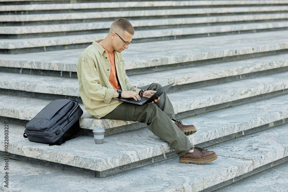 Poster side view of concentrated male it programmer in casual outfit using laptop to study or write code si