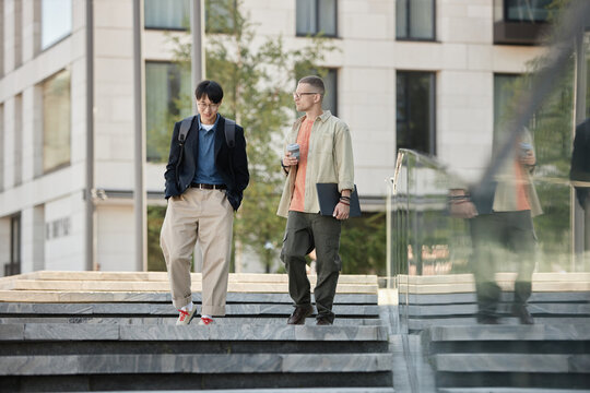 Full length shot of two male IT developers in stylish outfits talk business during walking meeting or daily commute to work while descending steps outside in city street, copy space