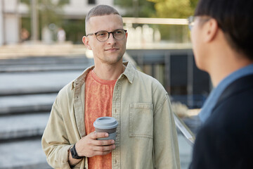 Medium shot of casually dressed man with reusable cup in hand meeting with friend or colleague...