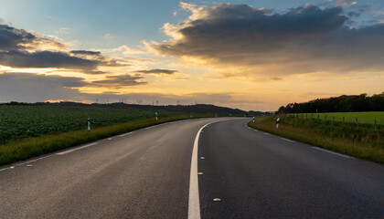 Naklejka premium winding road through fields at sunset under a colorful sky in a rural area with gentle hills