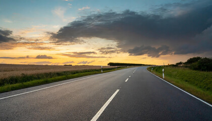 Naklejka premium A winding road through a serene landscape at sunset with dramatic clouds over a peaceful countryside