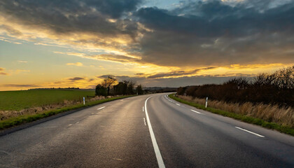 Naklejka premium A winding country road at sunset with a vibrant sky and grassy fields in the background