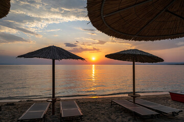 A wooden or plastic beach bed covering wooden reeds. In the background you can see the sea and a beautiful sunset.	