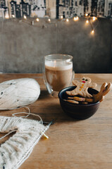 Gingerbread man cookies with coffee cup and white tweed knitting with needles. Decorated cookie with smile and eyes and wool yarn crocheting. Homemade biscuits with white knitting. 