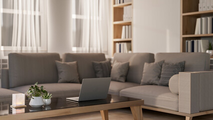 A laptop on a coffee table beside a large grey corner sofa in a contemporary living room.