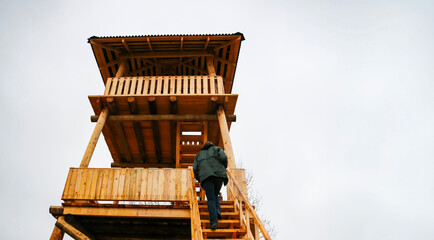 A person climbing wooden stairs toward a lookout tower in a rural area during cloudy weather