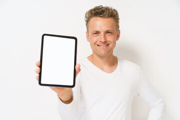 A man is holding a tablet in his hand and smiling. The tablet is black and white. The man is wearing a white shirt and has a beard