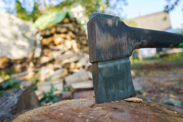A large axe is sitting on a log. The log is surrounded by a pile of wood. Concept of hard work and...
