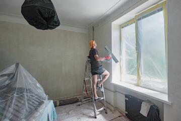 Amateur craftsman applying finishing putty on drywall with spatula. Man doing repair work with a...