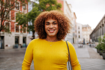 Latin gen z transgender woman smiling to the camera in city street.