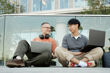 Candid shot of two smiling IT programmers from different ethnic backgrounds having fun while...
