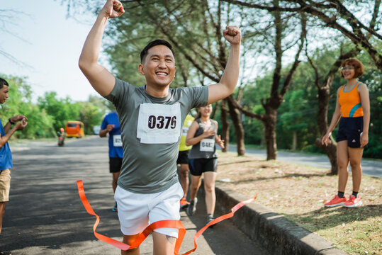 asian male runner crossing finish line celebrating victory with hands up gesture