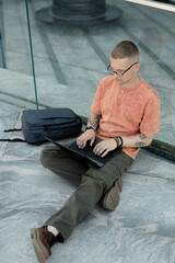 High angle shot of male IT programmer with backpack laying nearby using laptop to work while...