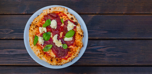Italian Pizza Manzo in a plate on a wooden table. Space for text.