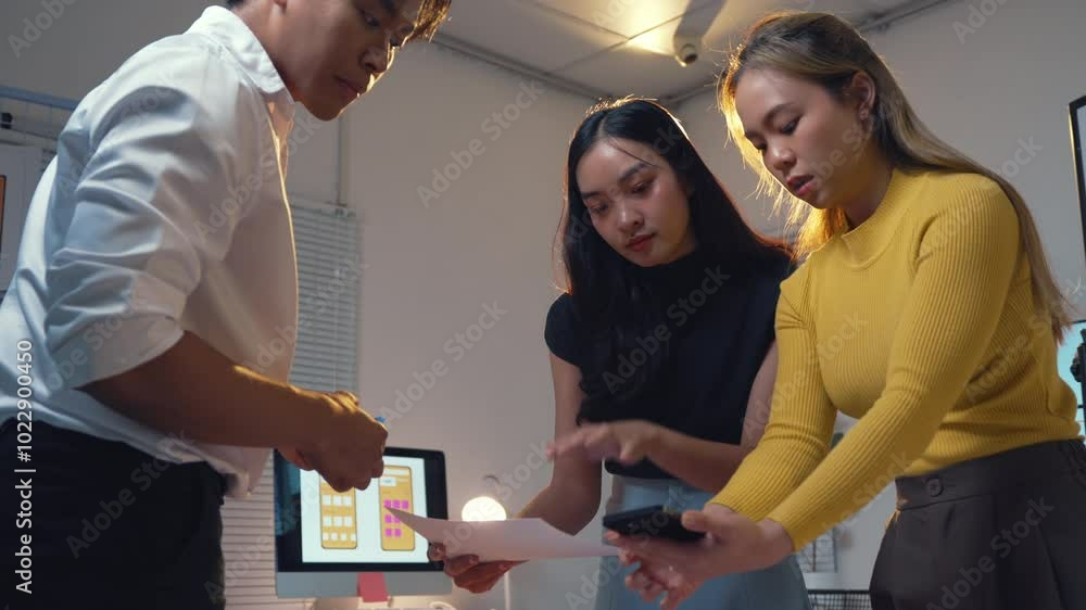 Poster designers collaborating late in the office, reviewing and discussing a mobile application design pro