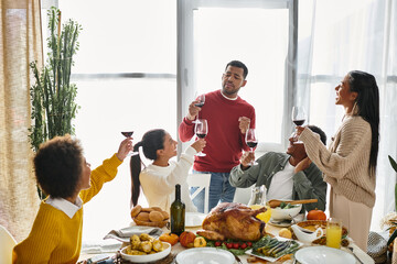 A group of friends raises glasses in a toast while enjoying a Thanksgiving feast together.