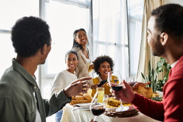 A group of friends gather around the table, sharing laughs and a delicious Thanksgiving meal.