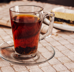 Steaming glass of black tea resting on tablecloth with cake in background