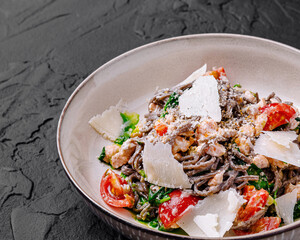 Black spaghetti with salmon, spinach and parmesan cheese lying on dark stone background