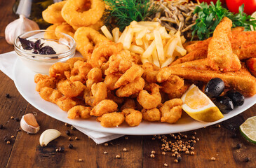 Large plate of delicious breaded seafood with french fries being served on wooden table