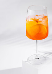 Aperol spritz cocktail standing on white cube casting shadow on white background