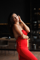 A brunette woman with beautiful thick hair with styling, Spanish. A tall girl in a red dress with a bare back in the bedroom, kitchen background. A charming lady has a beautiful athletic figure. smile