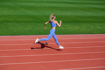 Fototapeta premium Woman in sportswear jogging on stadium. Female jogger runner running outdoors, runner. Fitness woman on stadium. Young fitness woman runner running on stadium track.