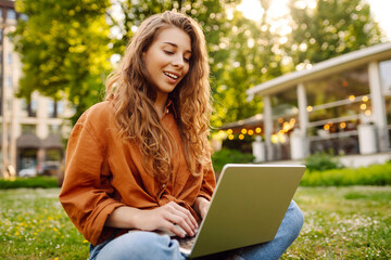 Happy woman with a laptop sitting on a green meadow. Education online. Freelance work, technology concept.