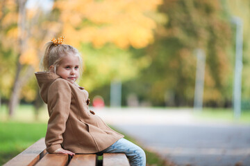 Thoughtful little girl sitting on bench in autumn park. Side view. Copy space.