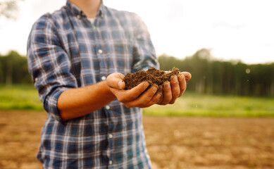 Close up of male hands touching soil on the field.  Farmer is checking soil quality before sowing....