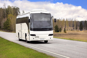White coach bus transports passengers along highway on a beautiful day of spring.