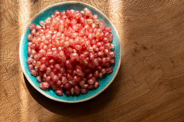 Fresh pomegranate seeds in a bowl on a wooden table shining in the afternoon sunlight. Perfect details.