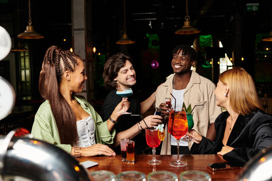 A cheerful group of young professionals enjoys cocktails and laughter at a corporate celebration.
