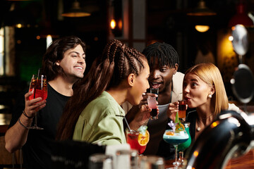 Young professionals enjoy colorful cocktails, laughing and chatting together.