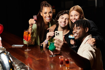 Four diverse colleagues enjoy drinks and laughter while capturing a joyful moment together.