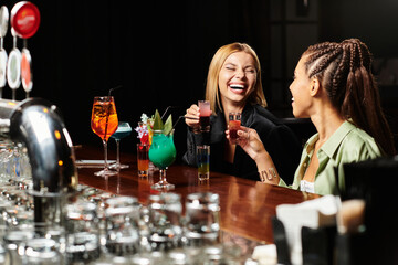 Two colleagues share laughter while toasting colorful cocktails at a festive corporate event.