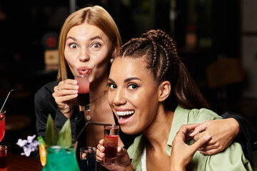 Two cheerful colleagues clink their drinks together, enjoying a fun moment at the party.