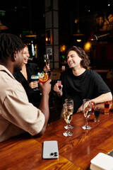 A diverse group of young colleagues enjoys drinks and laughter at a corporate celebration in a bar.