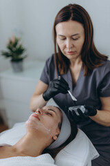 Cosmetologist performs a facial peeling procedure on a young woman.