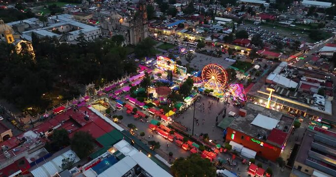 Orbital evening drone shot of the main square in the magical town of Tepotzotl&aacute;n, Mexico, featuring the fair set up in preparation for the municipal celebration during the month of September