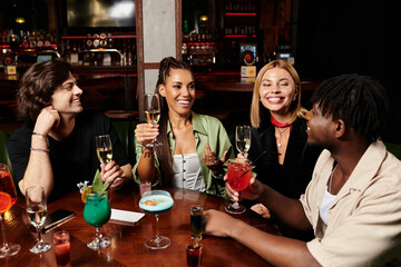 Four colleagues enjoy drinks and laughter at a lively corporate gathering, enhancing team spirit.