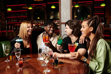 A lively group enjoys colorful cocktails and laughter during a corporate gathering at night.
